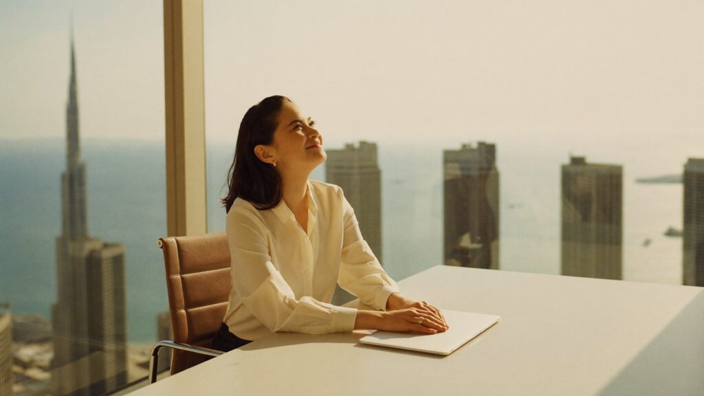 A woman pauses at a bright desk above the Dubai skyline, considering why UK reporting fund status matters to an expat investor.