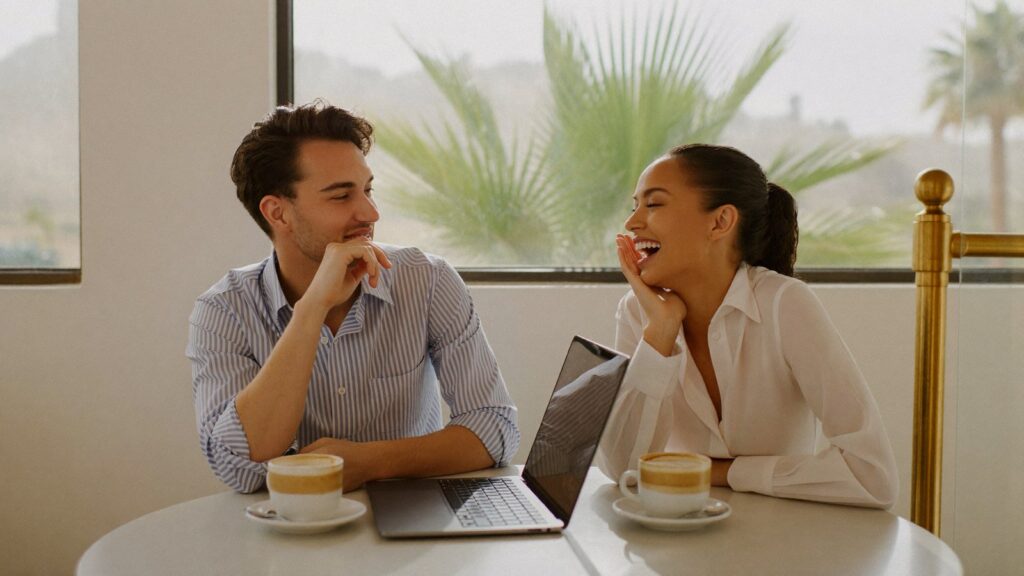 A young couple laugh over coffee and a laptop, weighing the four-year FIG regime on a return to the UK.