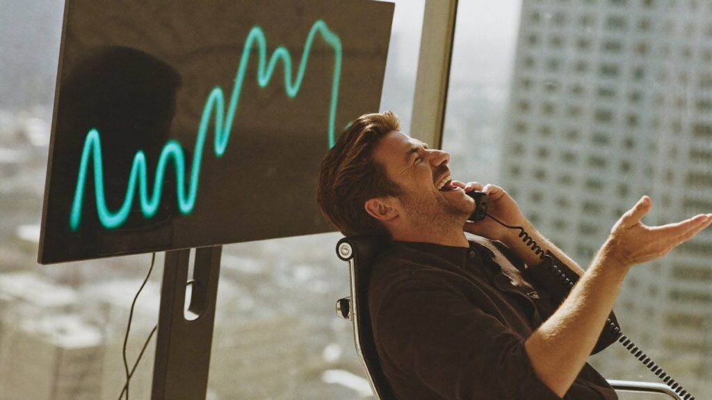 A man laughs on a call at his desk beside a glowing line chart, having moved a UK pension into a SIPP before relocating.