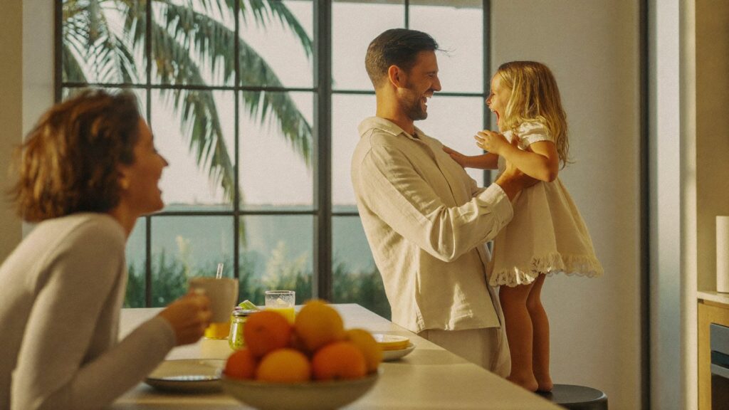 A father lifts his young daughter at a sunlit breakfast table, the family a UAE will is written to protect.